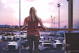 Woman stands at airport window looking at planes to depict travellers' tips for having a better flight.