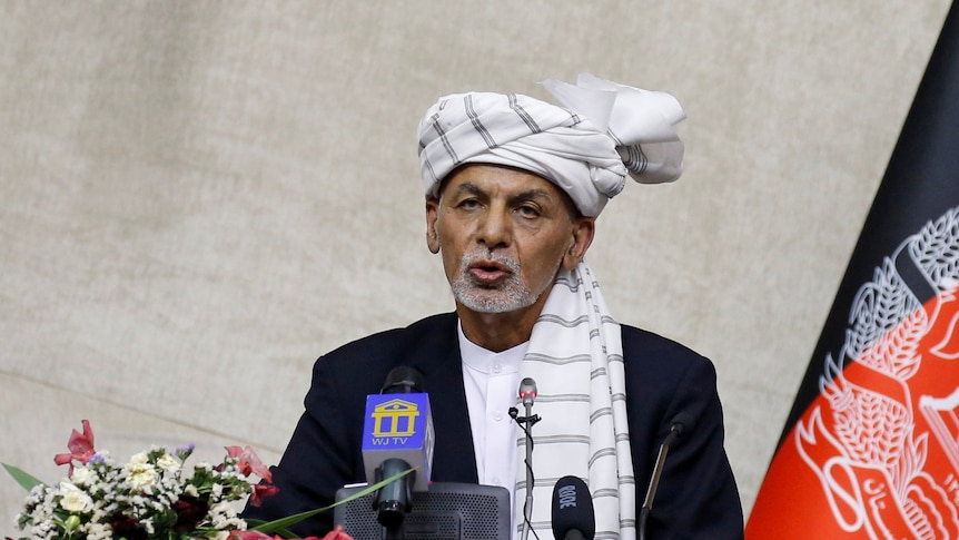 A man in a white head wrap speaks at a podium.