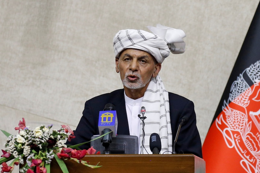 A man in a white head wrap speaks at a podium.