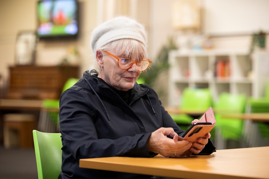 A woman in a jacket and beanie looks at her phone.