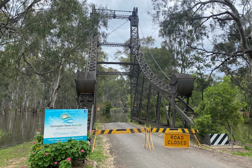 A steel structure at the entrance of a road or bridge with a road closed sign and water over the road.