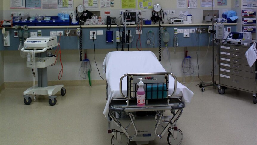 A hospital bed in a hospital room with medical devices on shelves behind it.