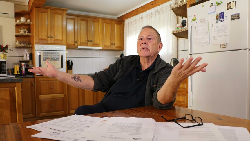 Garry Saville sits at home in his kitchen dealing with the paperwork for NDIS modifications at his home.