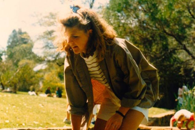 A young woman bending down in a park near a creek.