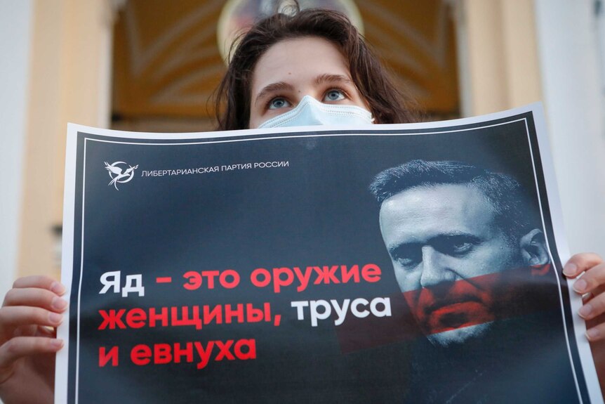 A protester stands holds a poster in Russian which reads "poison is the weapon of a woman, a coward and a eunuch!"