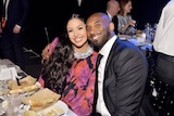 vanessa and kobe bryant sitting at a dining table smiling, kobe has his arm around vanessa and their faces are close together