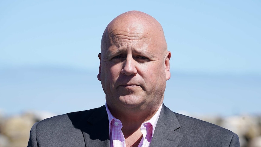 A bald man wearing a suit jacket and a pink shirt.