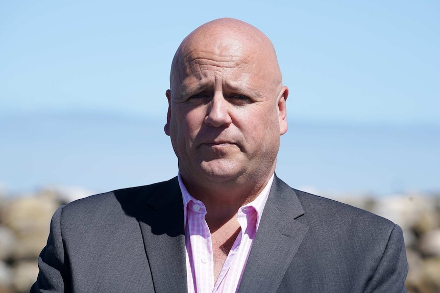 A bald man wearing a suit jacket and a pink shirt