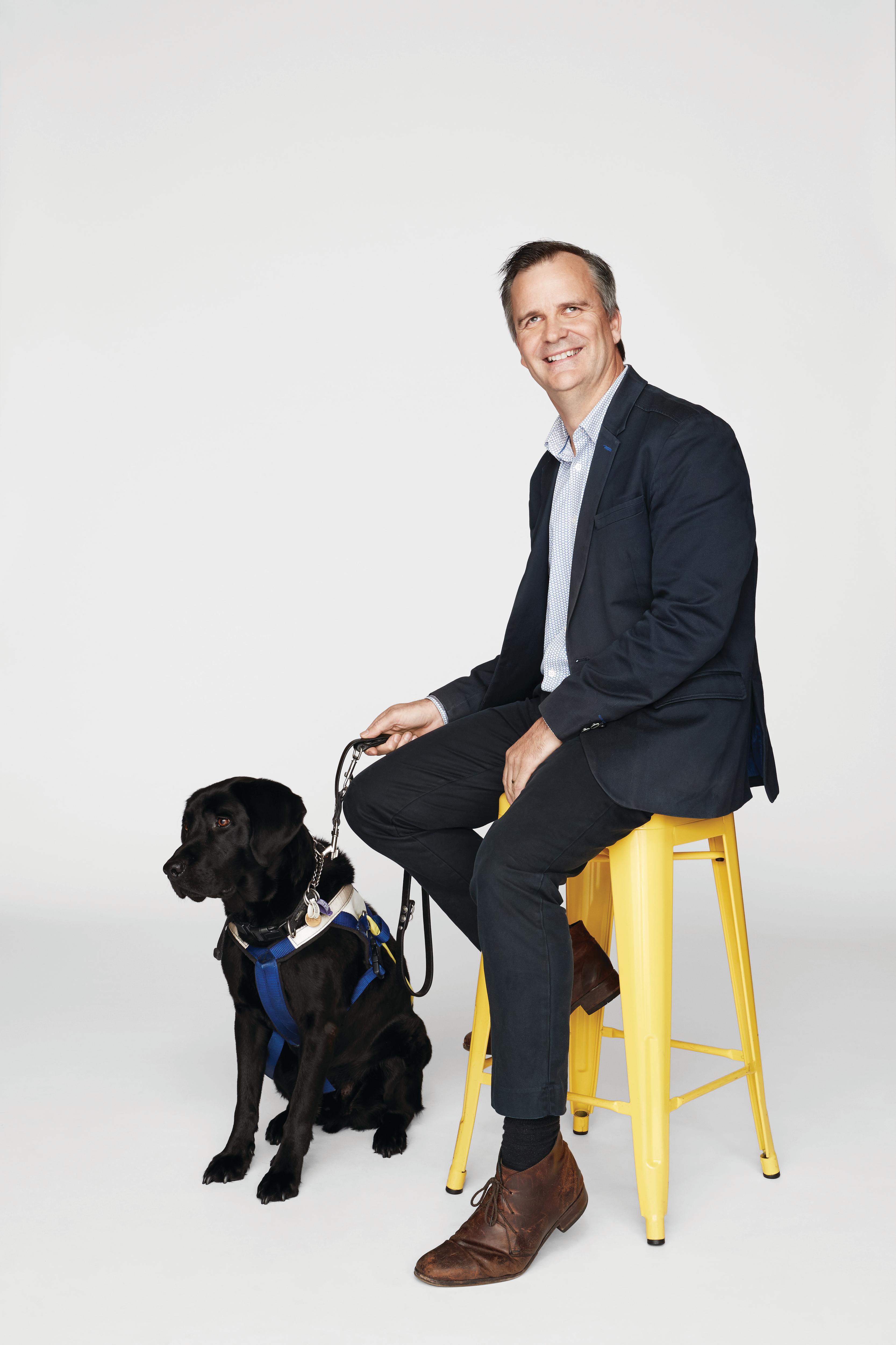 Chris Edwards sits on a stool while his Seeing Eye Dog, Odie, rests at his feet. 