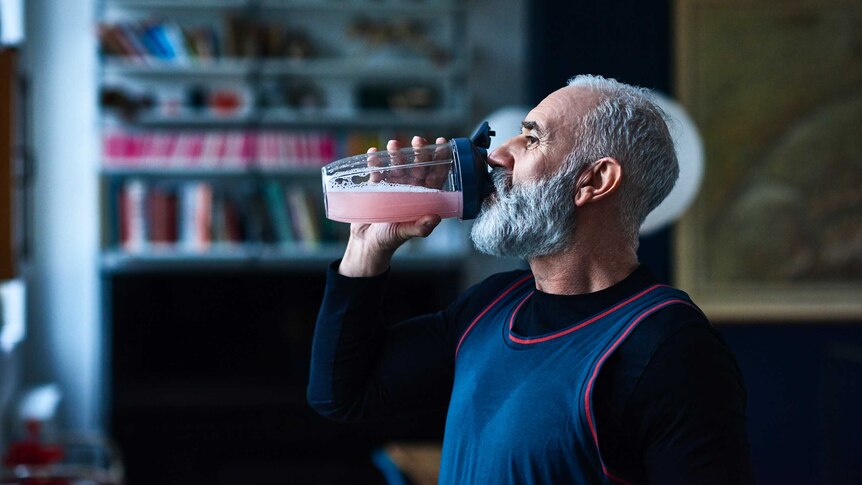 man with grey hair and beard drinks pink liquid from a shaker glass