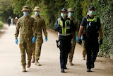 ADF personnel walk alongside Victoria Police officers, all masked and gloved, at The Tan walking track.