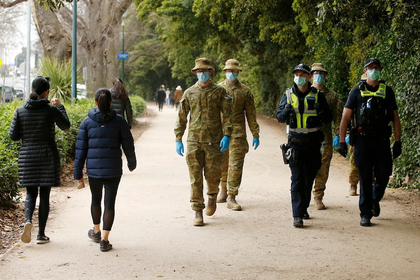 ADF personnel walk alongside Victoria Police officers, all masked and gloved, at The Tan walking track.