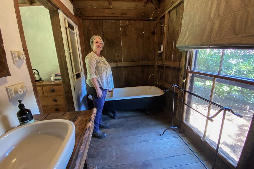 A woman stands in a rustic bathroom.