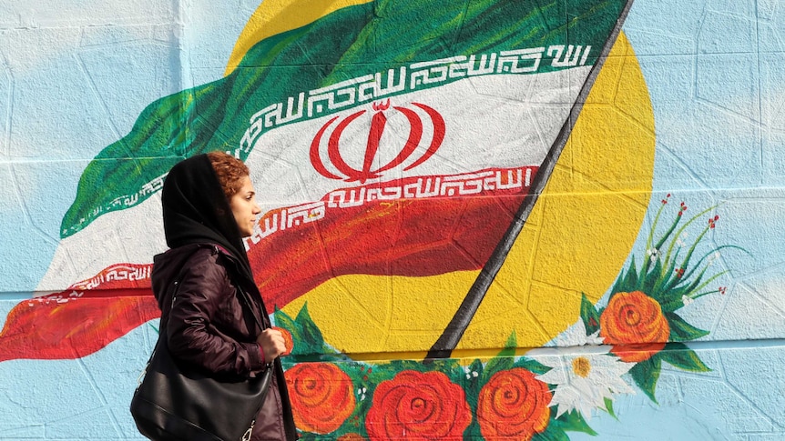 An Iranian woman walks past a mural painting of the Islamic republic's national flag.