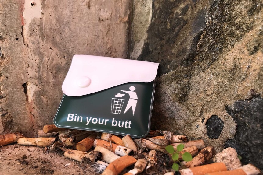 A small wallet sits on top of a pile of cigarette butts.