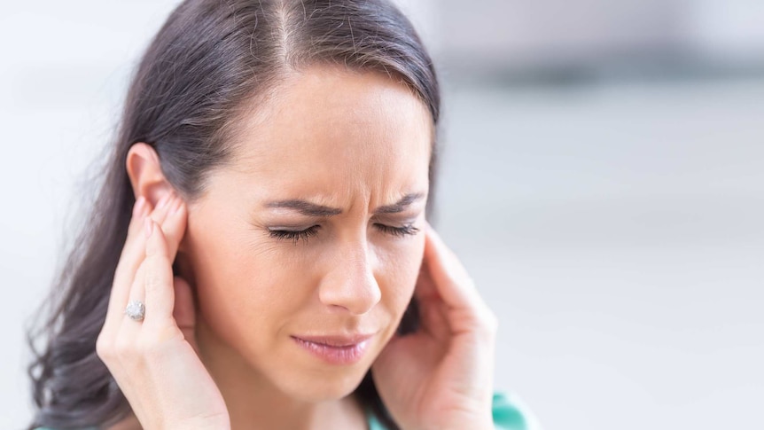 Person experiencing tinnitus holding ears in pain