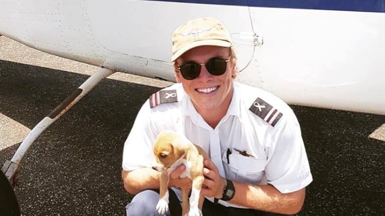 Young man kneels with puppy in front of plane.