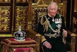 King Charles in full regalia seated next to the Queen's crown