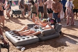 two men lounge on an inflatable bed in the middle of a dusty outdoor dancefloor