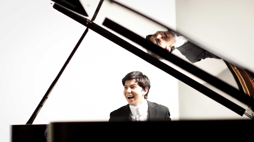 Smiling Uzbek pianist  Behzod Abduraimov seen between the piano lid and the side of piano