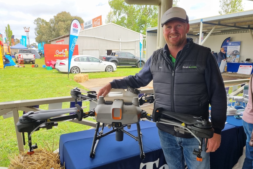 A bearded man standing next to an agriculture drone