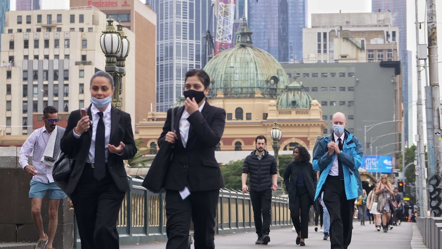 People walk across the bridge over the Yarra with Flinders Street Station in the background.