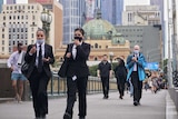 People walk across the bridge over the Yarra with Flinders Street Station in the background.