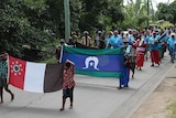 Parade on the street led by children and elders holding flags.