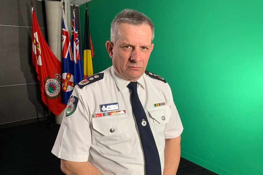 Man in uniform stands in front of an array of flags.