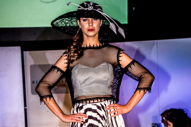 A front-on shot of a teen model wearing a black hat, mesh top and black and white striped skirt.
