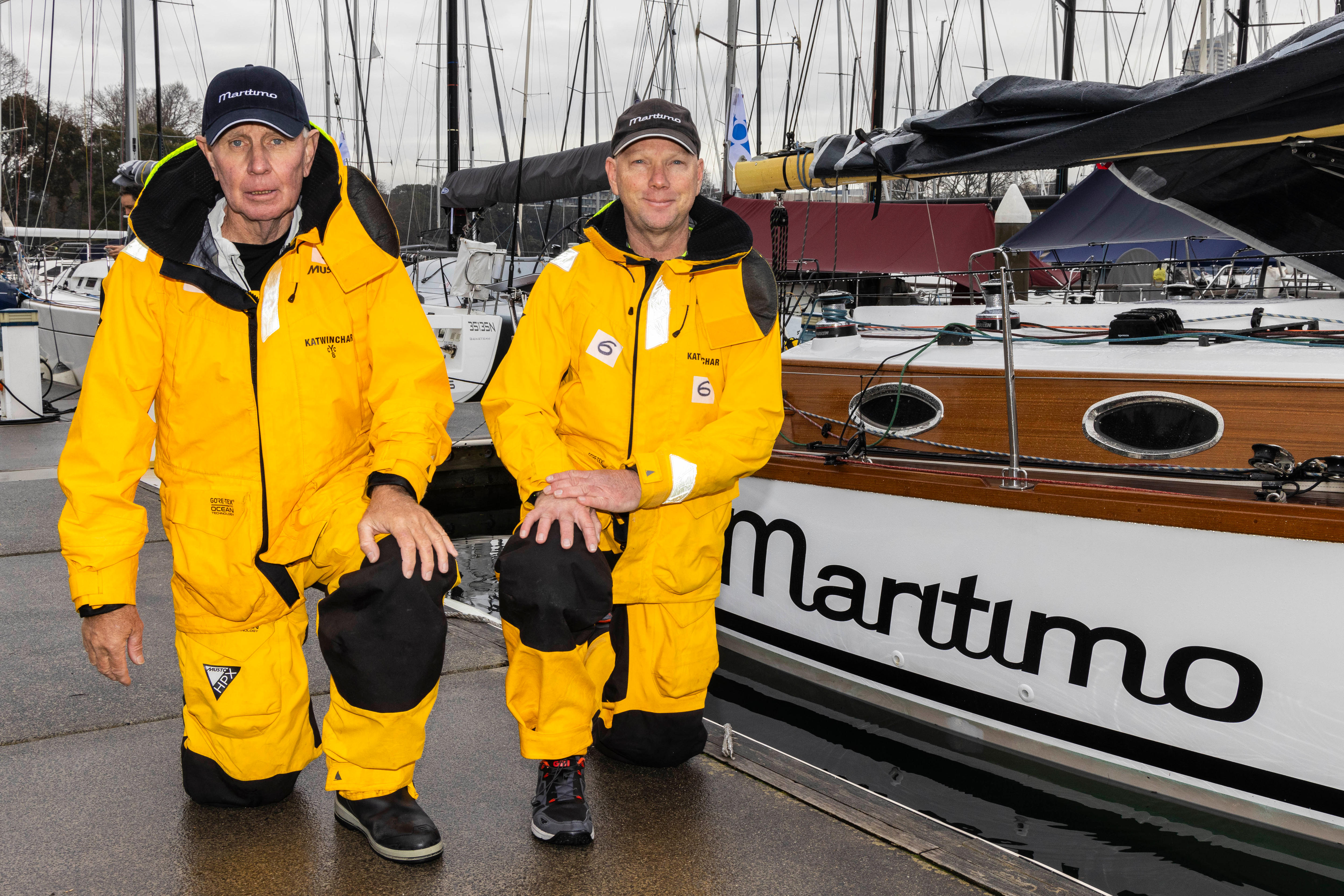 Dos hombres vestidos con ropa cálida y amarilla se arrodillan junto a un barco