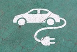 A white plogo of a car witha  power plug on a gree background. 