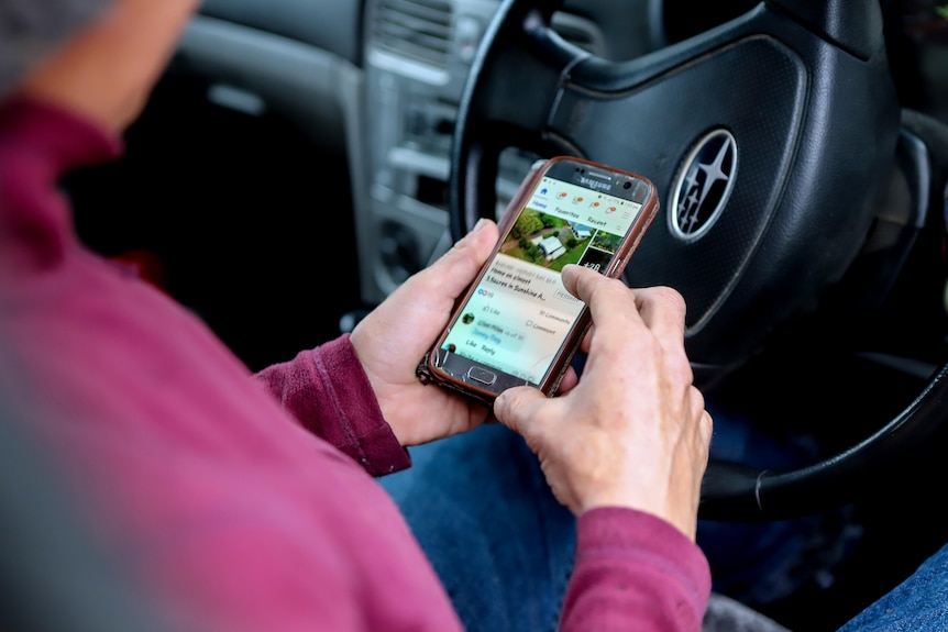 Woman in purple jumper flicks index finger on phone inside car with steering wheel visible 