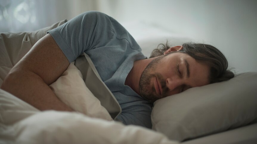 man with beard sleeping on his side under bed covers in t-shirt
