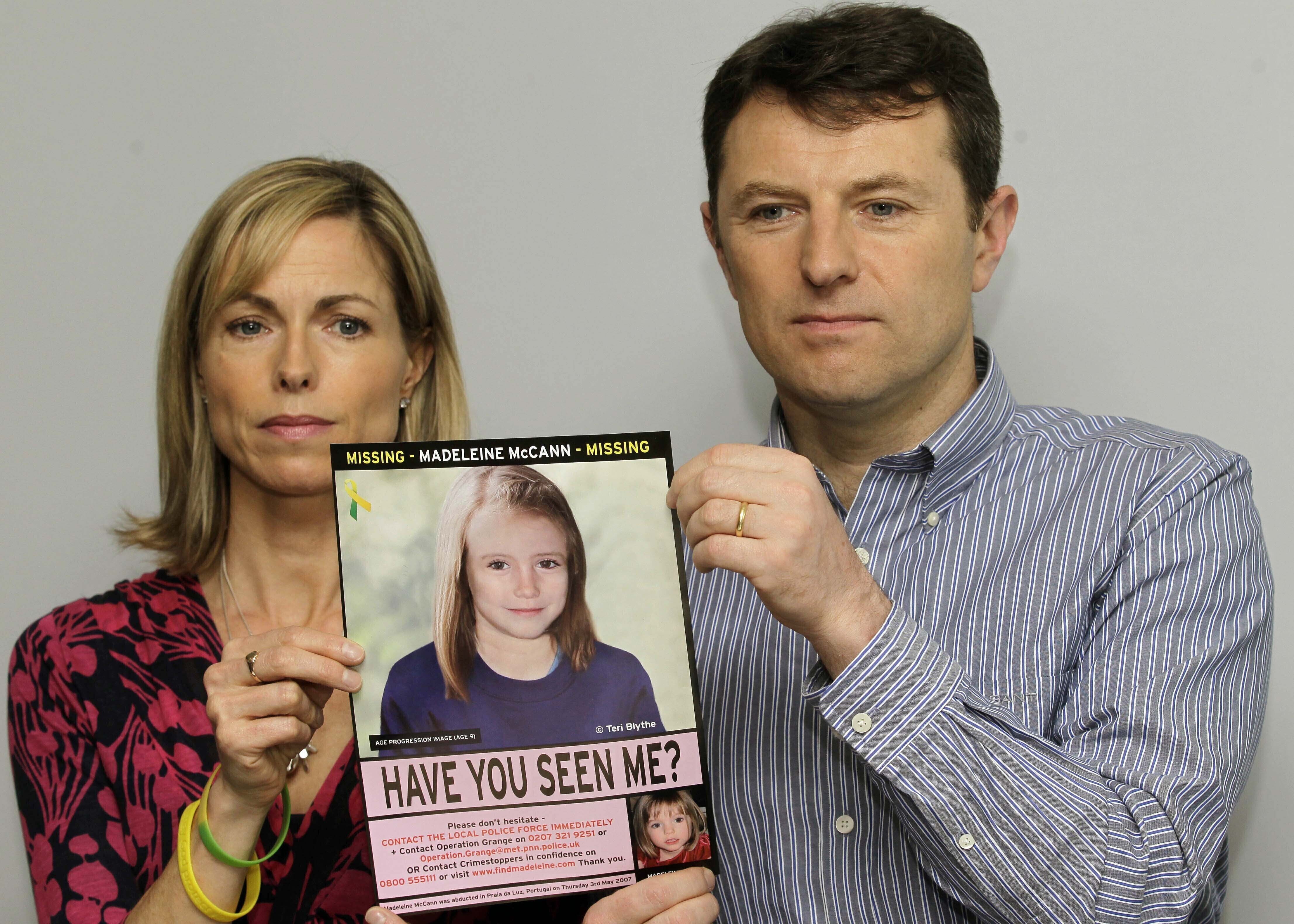 A middle-aged couple hold a poster of an illustration of their child as a teen.