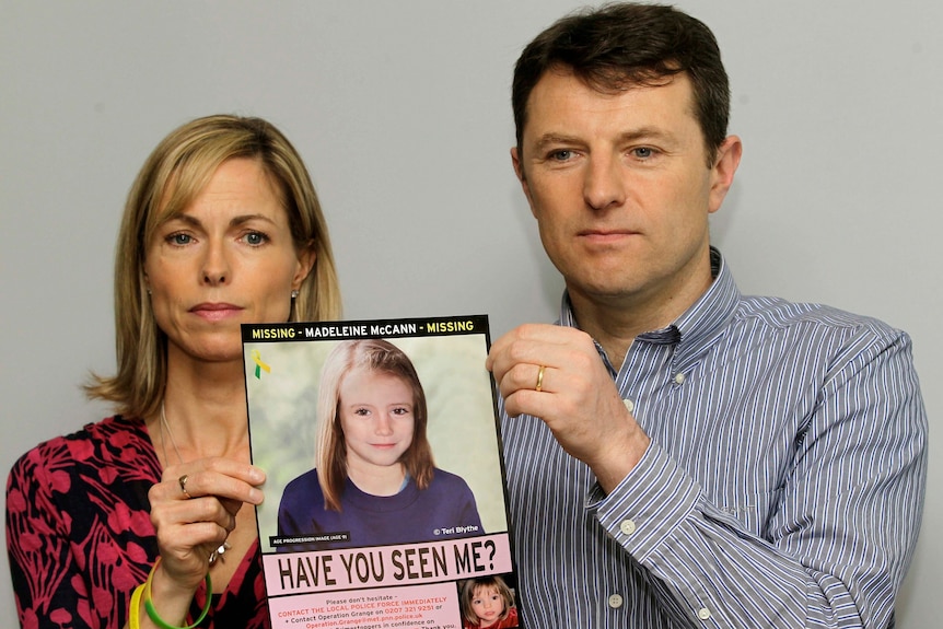 A middle-aged couple hold a poster of an illustration of their child as a teen.
