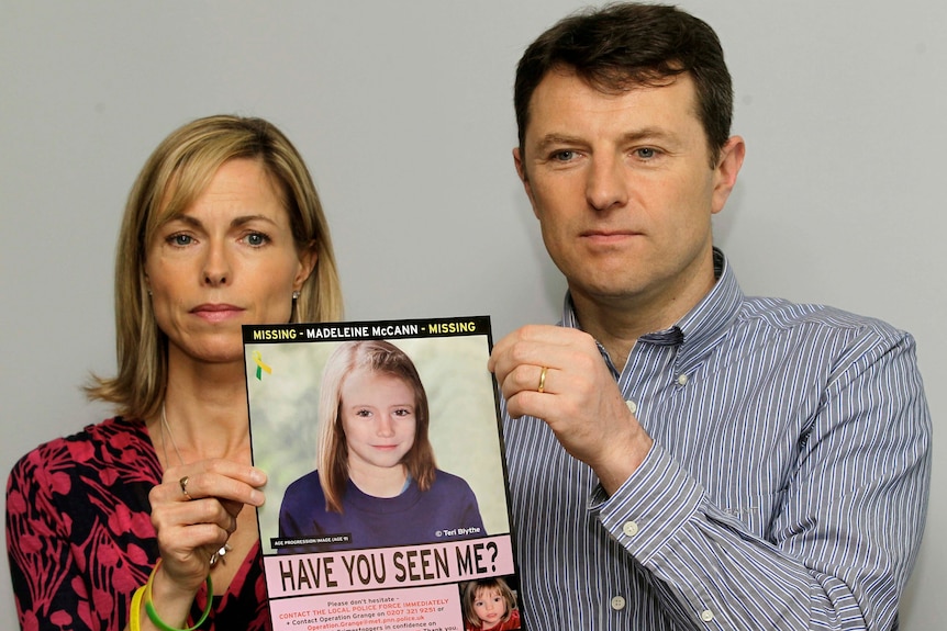 A middle-aged couple hold a poster of an illustration of their child as a teen.