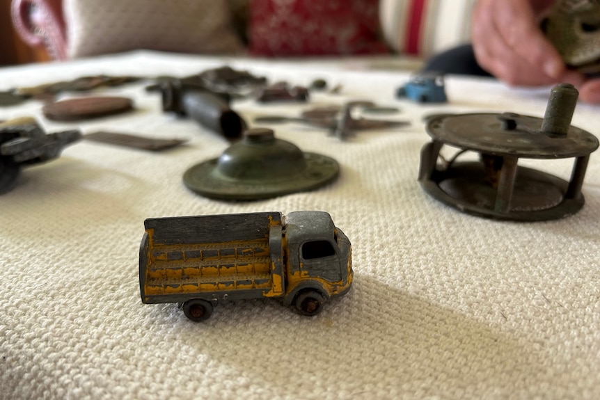 A small, rusted toy truck is seen on a table, along with old coins and other objects.