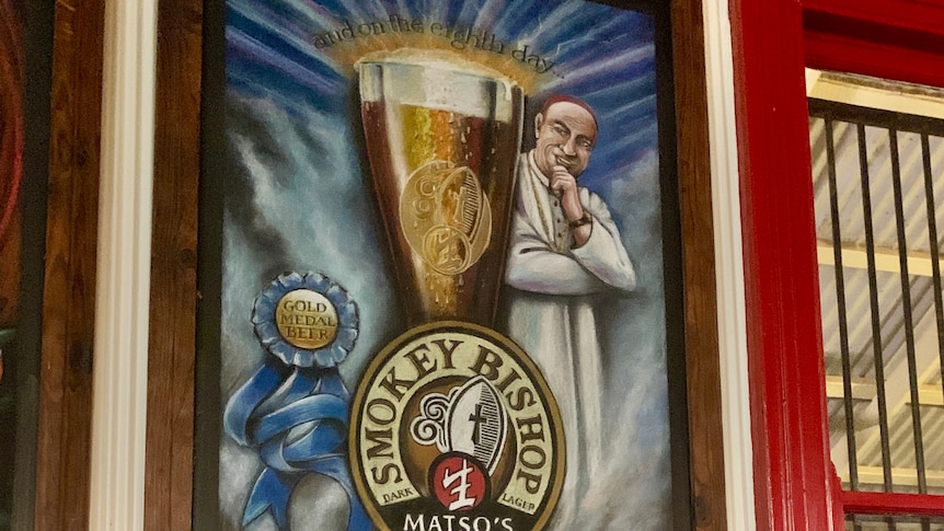 A large advertising image of a Catholic cleric smiling next to a large glass of beer, hanging on a wall