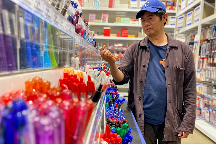 A man in a blue cap selects a pen from clusters of different coloured ones stacked in rows. 