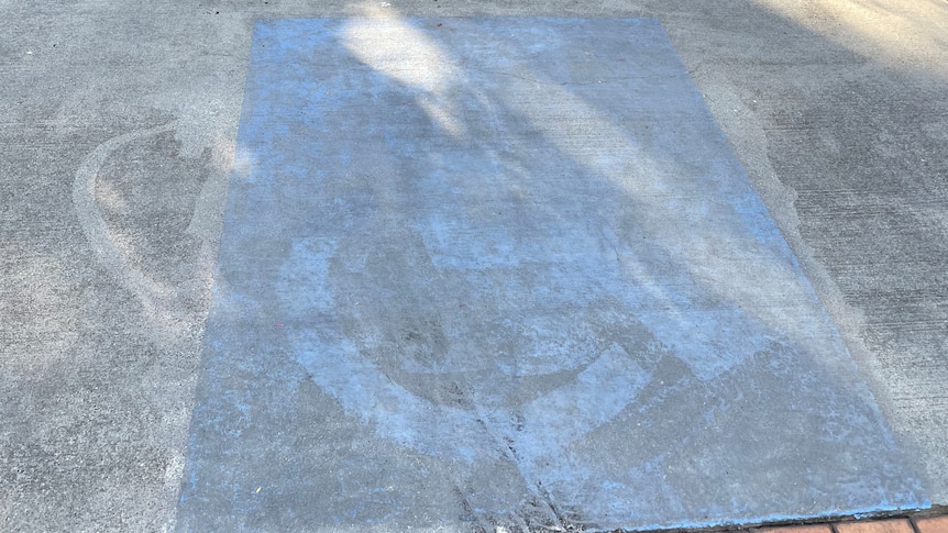 A faded blue square and wheelchair symbol in a car park space.