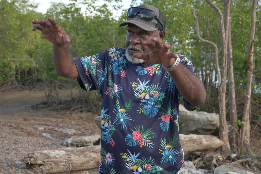 A man wearing a patterned t-shirt with raised arms in front of a mangrove