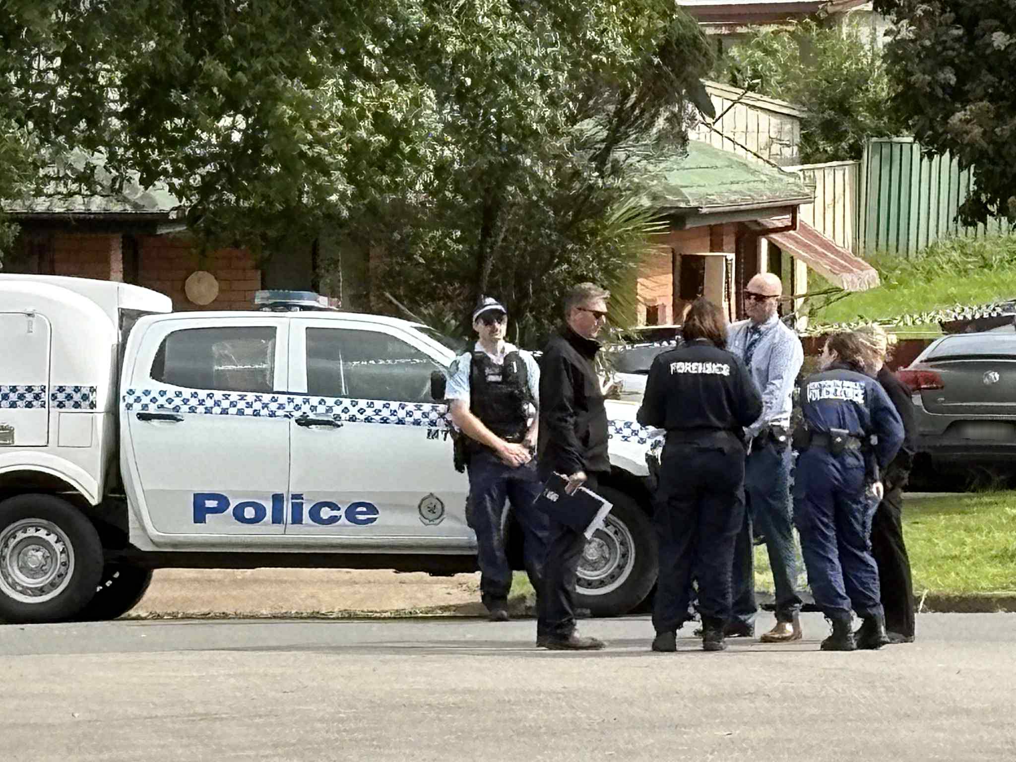 A group of police stand in front of a police car on a street. 