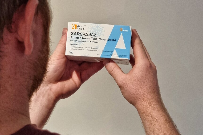 photo showing back of man's head and his hands holding a box of rapid antigen tests