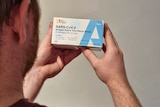 photo showing back of man's head and his hands holding a box of rapid antigen tests