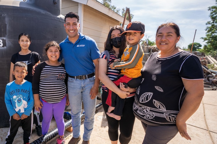 A family stands smiling next to a big, black water tank 