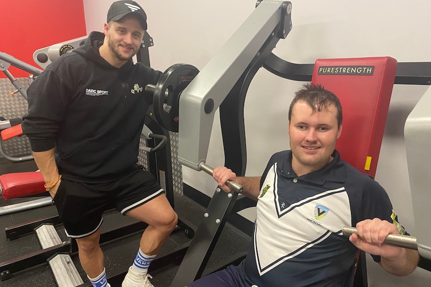 Man at the gym standing next to another man using equipment 