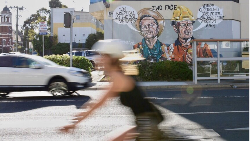 A blurred cyclist rides past a large mural in Preston depicting Bill Shorten.
