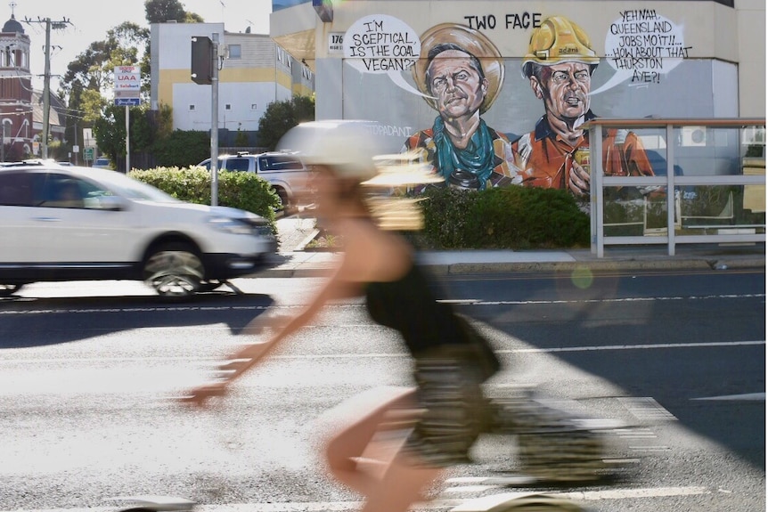 A blurred cyclist rides past a large mural in Preston depicting Bill Shorten.