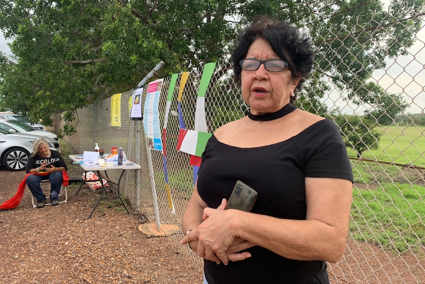 a woman wearing a black top in front of a mesh fence